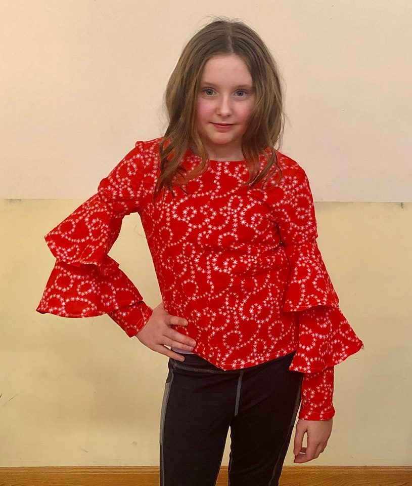 A little girl wearing a red structured top